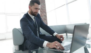 ofis lobisinde otururken dizüstü bilgisayar üzerinde çalışan iş adamı