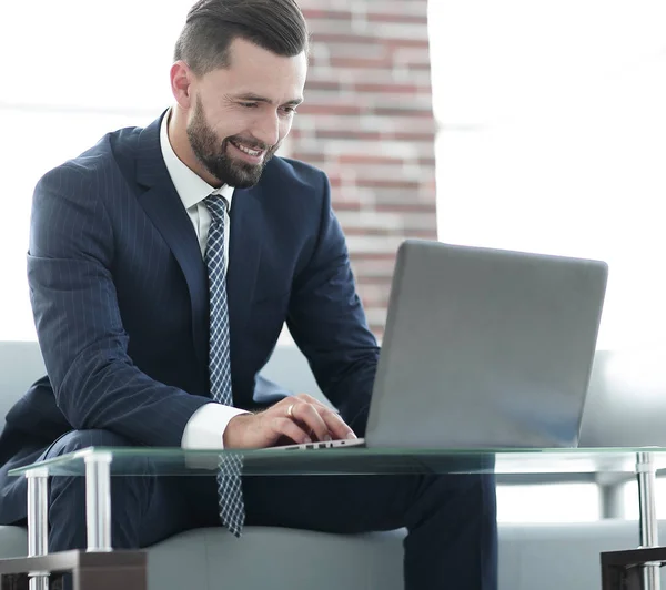 Empresário trabalhando em laptop sentado em um sofá em um escritório — Fotografia de Stock