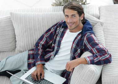 dizüstü bilgisayarda çalışan ve kameraya bakarak bir genç adam. Yukarıdan görüntülemek