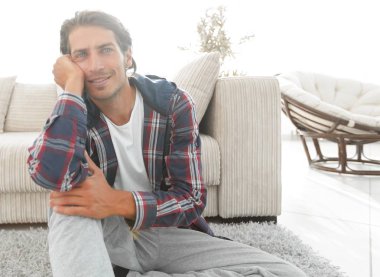 Kendine güvenen adam rahat bir oturma odasında halı üzerinde oturan.