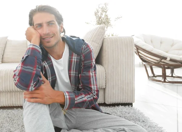 Kendine güvenen adam rahat bir oturma odasında halı üzerinde oturan.