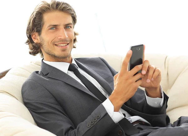 Homem de negócios de sucesso com um smartphone sentado em uma cadeira confortável — Fotografia de Stock