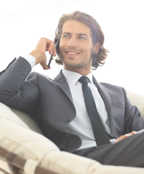 Hombre de negocios hablando en un teléfono inteligente mientras está sentado en una silla cómoda . — Foto de Stock