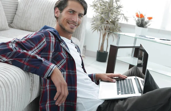 Encantador jovem com laptop sentado na sala de estar moderna — Fotografia de Stock