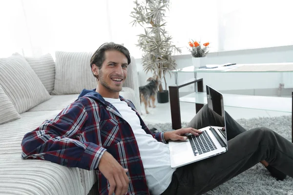 Charmanter junger Mann mit Laptop sitzt im modernen Wohnzimmer — Stockfoto