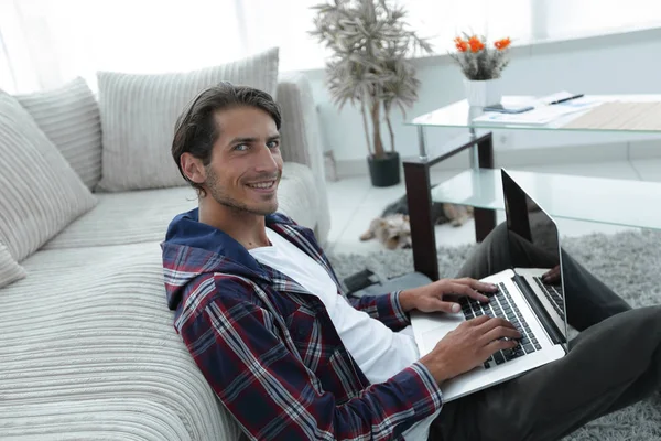 gülümseyen adam kanepede yakın katta oturan bir dizüstü bilgisayar ile