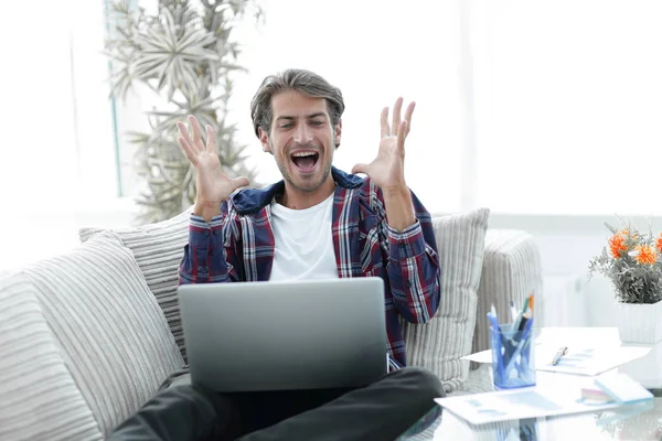 Heureux jeune homme réussi regardant ordinateur portable à la maison . — Photo