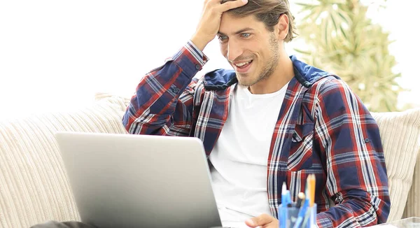 Χαρούμενος νεαρός άνδρας που εργάζεται με φορητό υπολογιστή από το σπίτι. — Φωτογραφία Αρχείου
