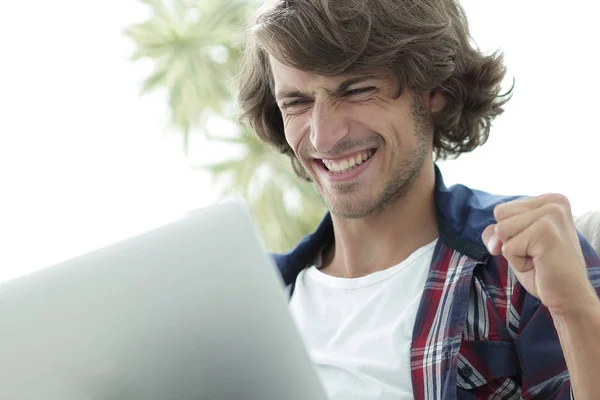 Chico muy feliz con un portátil sentado cerca de una mesa de café . — Foto de Stock