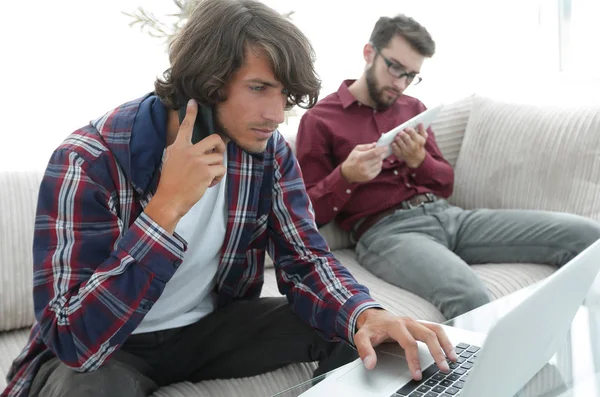 Two guys sitting on the couch, talking on the smartphone and communicating on the Internet. — Stock Photo, Image