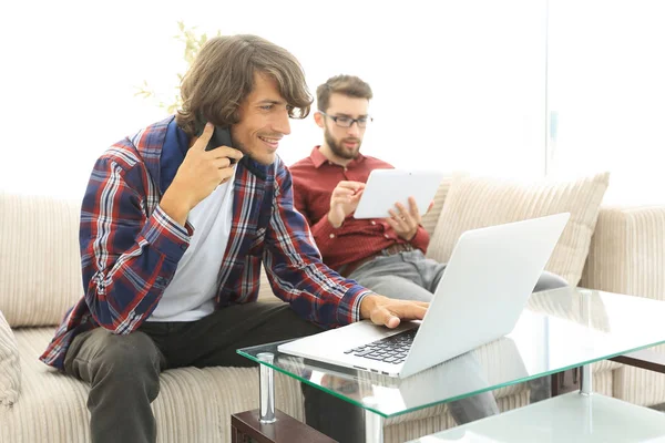 Deux gars assis sur le canapé, parlant sur un téléphone portable et bavardant sur Internet . — Photo