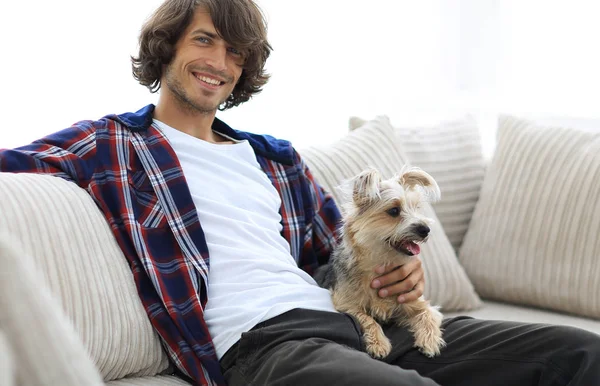 Snygg kille sitter i soffan med sin hund. — Stockfoto