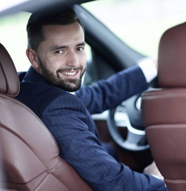 bir araba direksiyon başında oturan ve kameraya bakarak işadamı