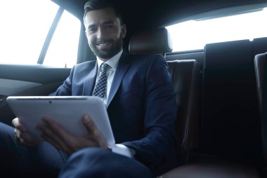 bir arabanın arka koltuğunda çalışma ve bir tablet kullanarak iş adamı