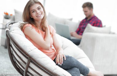 Güzel genç bir kadın büyük, rahat bir sandalyede oturuyor.