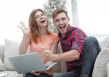 Genç çift sevinir, açık belgili tanımlık laptop önünde kanepede oturan