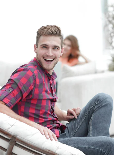 Šťastný mladý muž sedí ve velkém křesle na rozmazaném pozadí — Stock fotografie