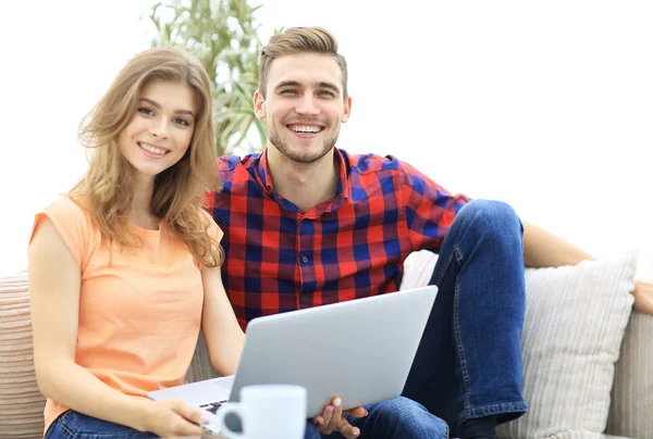 Young couple of students uses a laptop sitting on sofa — Stock Photo, Image