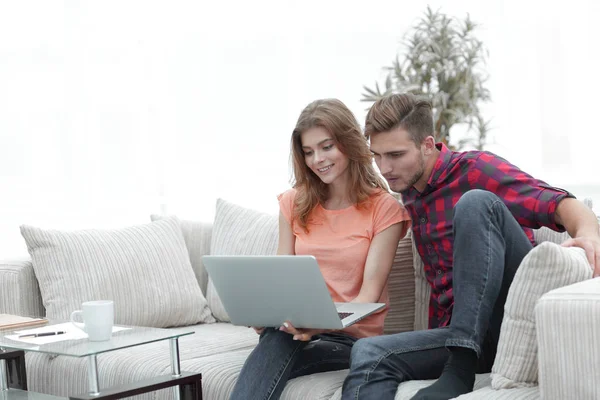 Jovem com sua namorada olhando para o laptop sentado no sofá . — Fotografia de Stock