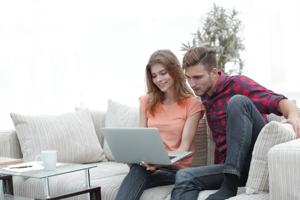 Young man with his girlfriend looking at the laptop sitting on the sofa. — Stock Photo, Image