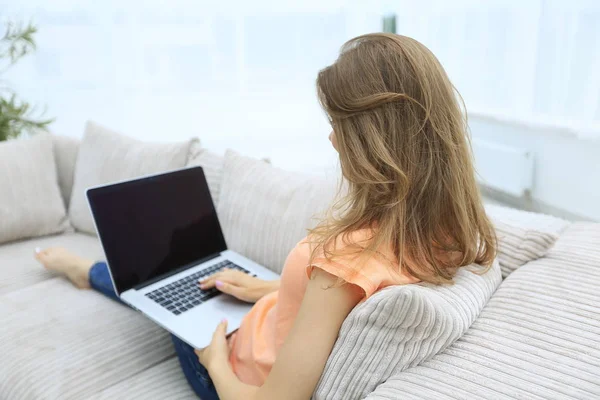 Молодая женщина работает с ноутбуком сидя на диване — стоковое фото