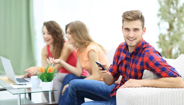 Moderní chlap s chytrým telefonem a jeho přátelé sedí na gauči — Stock fotografie