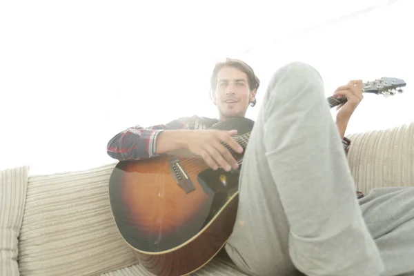 Парень с гитарой сидит на диване в гостиной. концепция образа жизни — стоковое фото