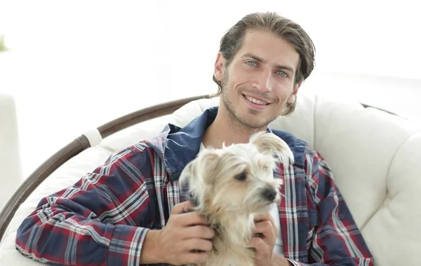 Close-up of a smiling guy stroking his dog while sitting in a large armchair. — Stock Photo, Image