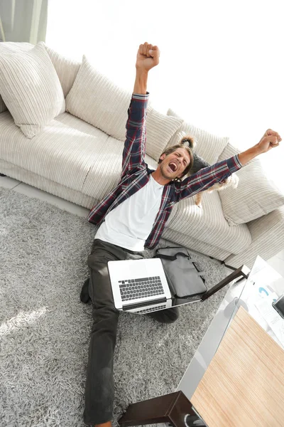 Glücklicher Kerl mit Laptop jubelt im geräumigen Wohnzimmer. — Stockfoto
