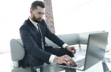 ofis lobisinde otururken dizüstü bilgisayar üzerinde çalışan iş adamı