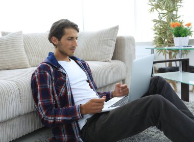 Modern adam kanepede yakın katta oturan bir dizüstü bilgisayar ile