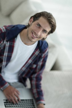 dizüstü bilgisayarda çalışan ve kameraya bakarak bir genç adam. Yukarıdan görüntülemek