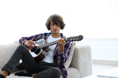 Yakışıklı adam evde kanepede gitar çalmaya