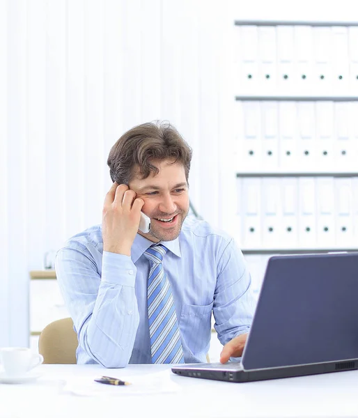 Knappe zakenman zit aan Bureau en praten op een mobiele telefoon — Stockfoto