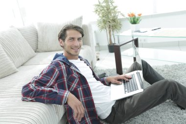 kanepede yakın katta oturan dizüstü bilgisayar ile gülümseyen genç adam