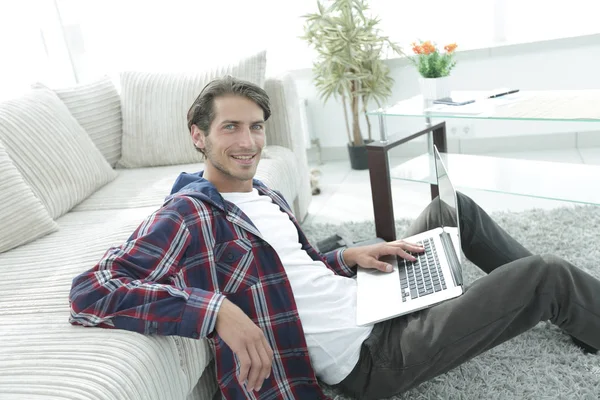 kanepede yakın katta oturan dizüstü bilgisayar ile gülümseyen genç adam