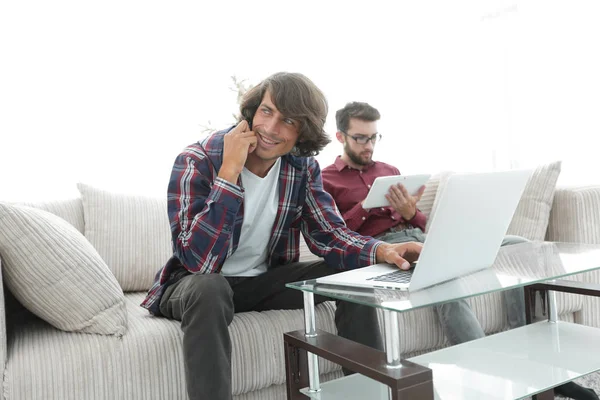 Dos tipos sentados en el sofá, hablando en el teléfono inteligente y comunicándose en Internet . —  Fotos de Stock