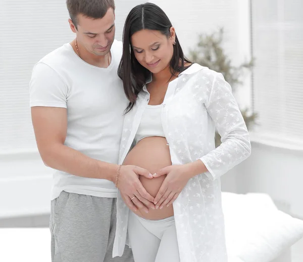 Marido y mujer embarazada con las manos dobladas en forma de corazón en la barriga — Foto de Stock
