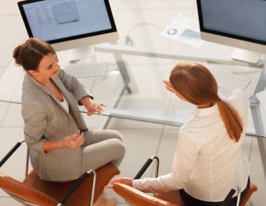 Üst kattan manzara. İş kadını, masaüstünde oturan bir meslektaşıyla konuşuyor.