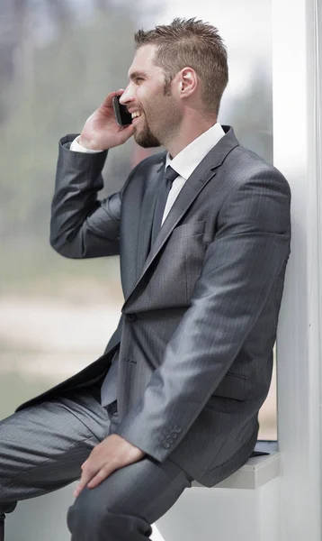Empregado falando ao telefone, sentado no peitoril da janela — Fotografia de Stock