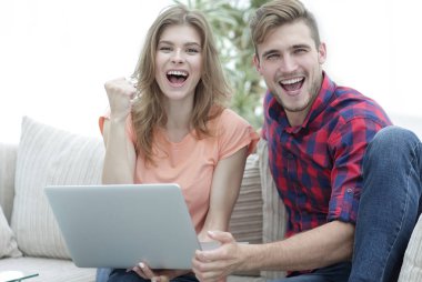Genç çift sevinir, açık belgili tanımlık laptop önünde kanepede oturan