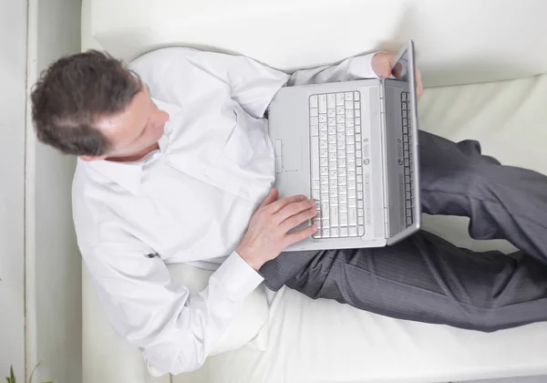 Pohled z top.man pracují na notebooku, ležící na pohovce. — Stock fotografie