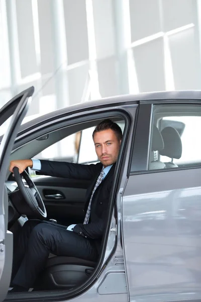 Businessman sitting behind the wheel of a car, in the Parking lot at the car dealership — Stock Photo, Image