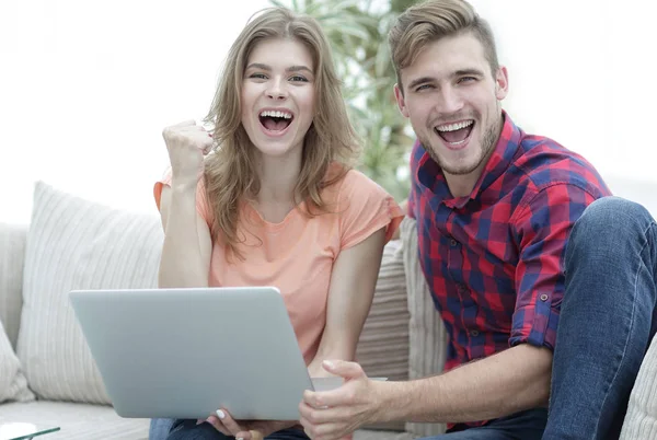 Genç çift sevinir, açık belgili tanımlık laptop önünde kanepede oturan