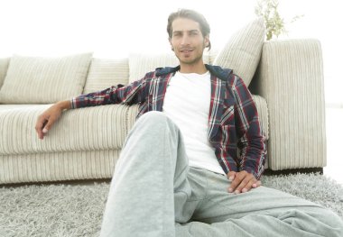 Kendine güvenen adam rahat bir oturma odasında halı üzerinde oturan.