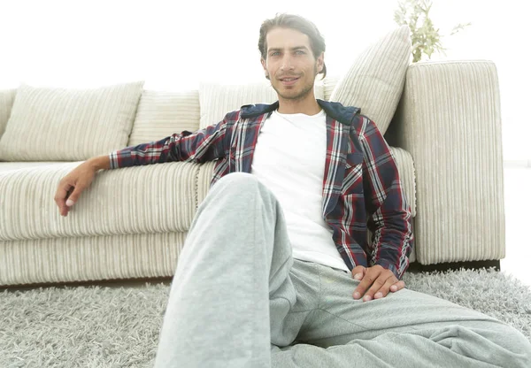 Kendine güvenen adam rahat bir oturma odasında halı üzerinde oturan.