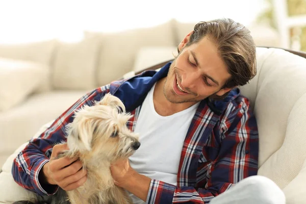 Stilig kille strök hans hund när man sitter i en stor fåtölj. — Stockfoto