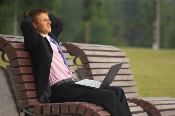 Mladý podnikatel se sedět v parku a pomocí přenosného počítače — Stock fotografie