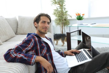 modern oturma odasında otururken dizüstü bilgisayar ile büyüleyici genç adam