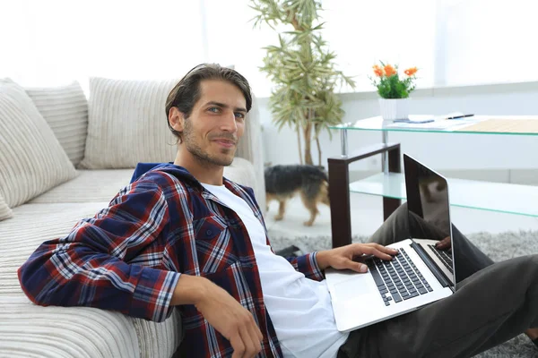 modern oturma odasında otururken dizüstü bilgisayar ile büyüleyici genç adam